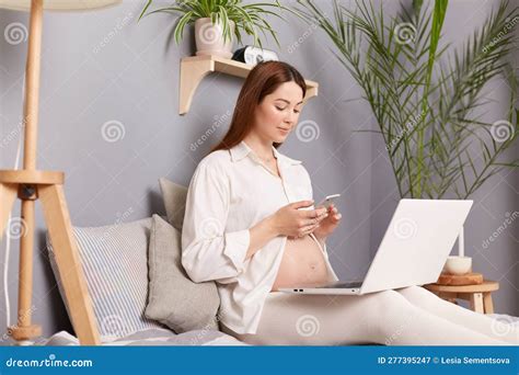 Brown Haired Pregnant Woman Sitting On Bed Using Computer At Home