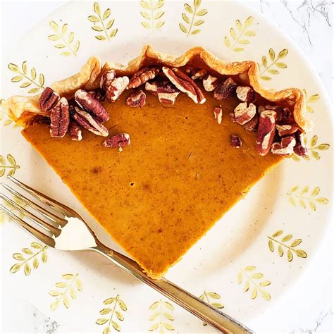 A wedge of pumpkin eggnog pie on a beige plate with a rim decorated by ...