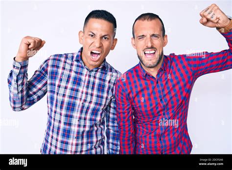 Joven pareja gay de dos hombres con ropa casual enojado y enojado levantar el puño frustrado y
