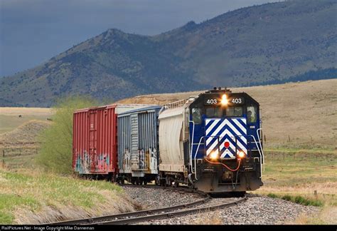 A Train Traveling Down Tracks Next To A Lush Green Field And Mountain