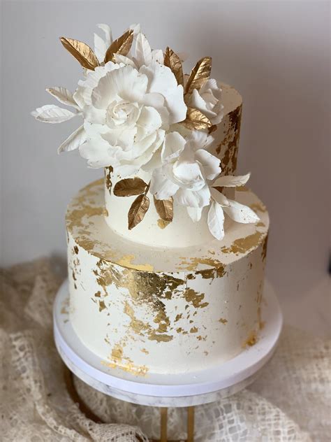 A White And Gold Wedding Cake With Flowers On Top