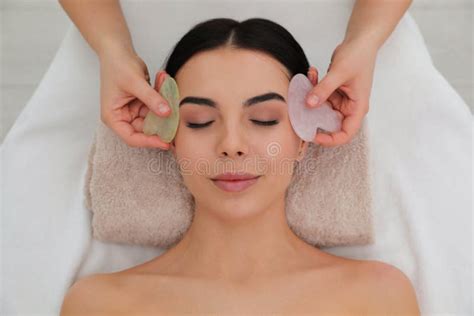 Young Woman Receiving Facial Massage With Gua Sha Tools In Beauty Salon