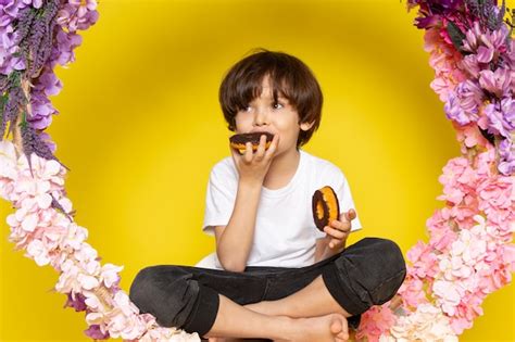 Una Vista Frontal Chico Lindo Comer Donas Alrededor De Flores En El