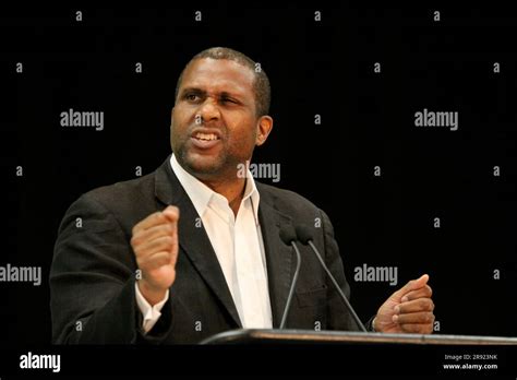 A Young Caucasian Man Stands Confidently In Front Of A Microphone On A Stage Addressing A Crowd