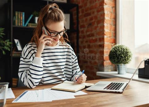 Pensive Pleased Woman Writing In Notepad While Making Phone Call In