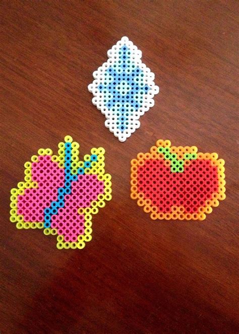 Three Pieces Of Perler Bead Art On A Wooden Table With One Piece Cut