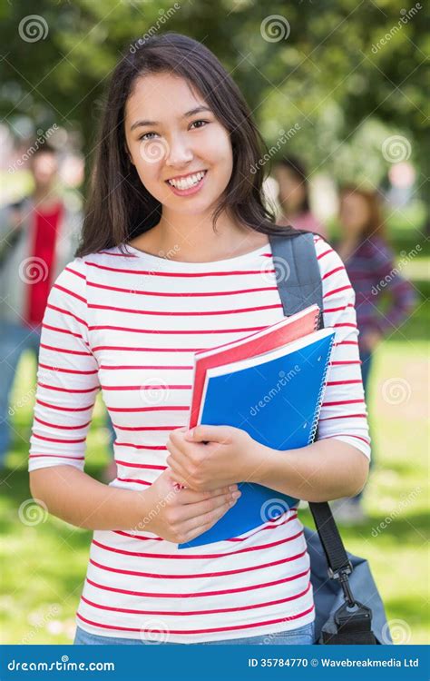 College Girl Holding Books With Blurred Students In Park Stock Photo