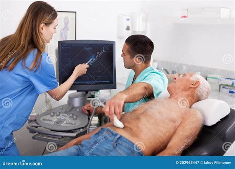 Skilled Doctor With Assistant Diagnosing Patient Using Ultrasonography Scanner In Private Clinic