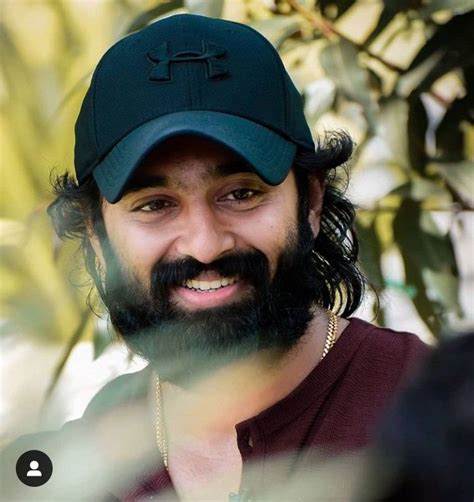 A Man With Long Hair And A Beard Wearing A Green Hat Smiles At The Camera