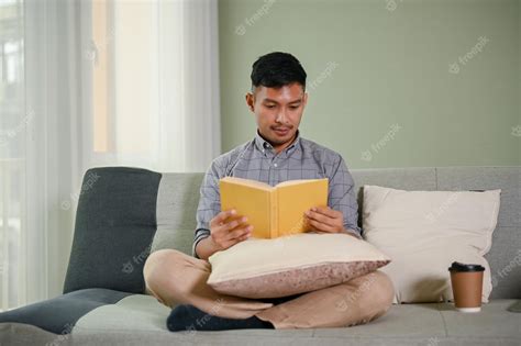 Premium Photo Smart And Positive Millennial Asian Man Reading Book On Sofa In His Living Room