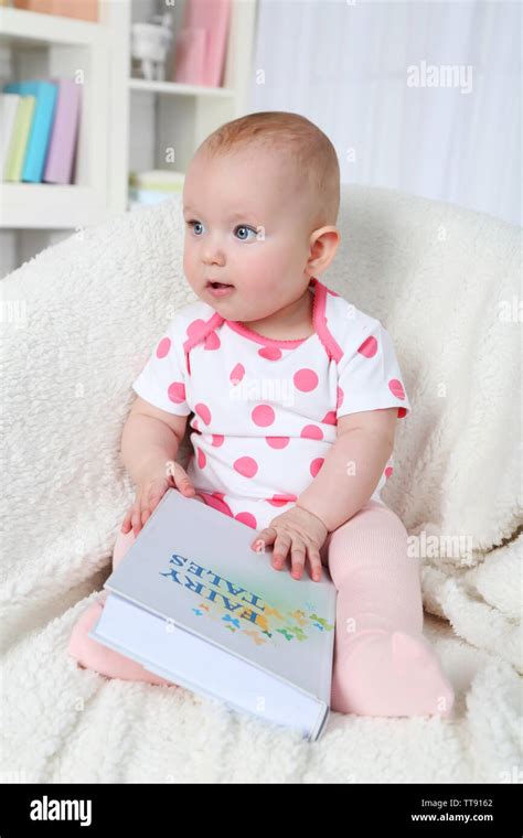 Cute Baby Girl Sitting In Arm Chair With Book On Home Interior