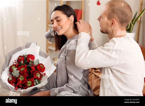 Young Man Putting Necklace Around His Wifes Neck In Bedroom On