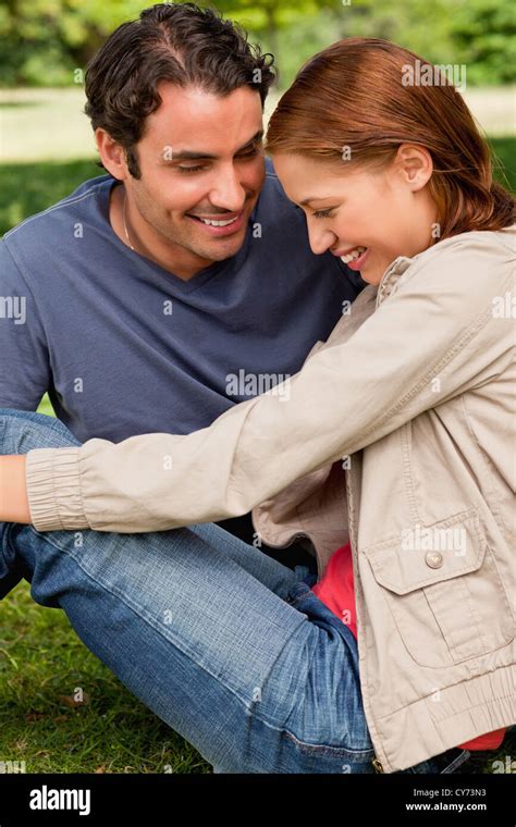 Two Friends Look Happily Towards The Ground As They Sit Next To Each