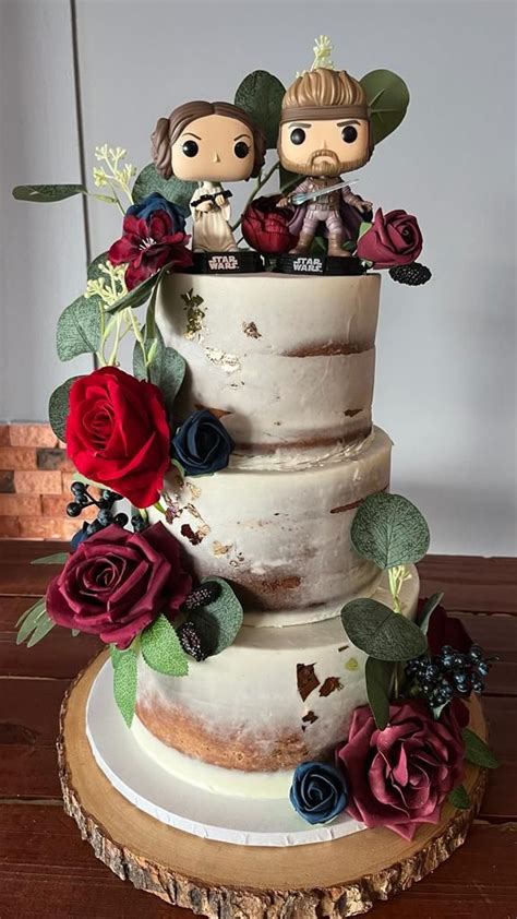 Two Figurines Are Sitting On Top Of A Three Tiered Cake With Flowers