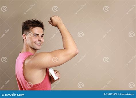 Young Man Applying Deodorant To Armpit On Beige Background Stock Photo