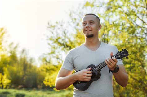 Premium Photo Young Man Stands Playing Ukulele In Park