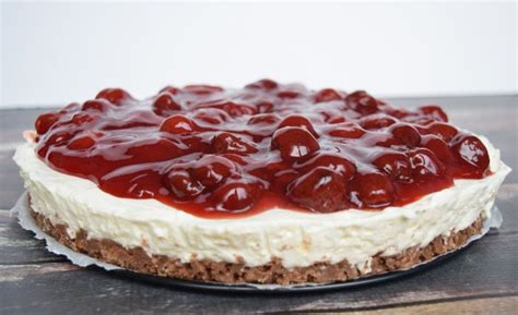 A Cheesecake Covered In Cherries On Top Of A Wooden Table