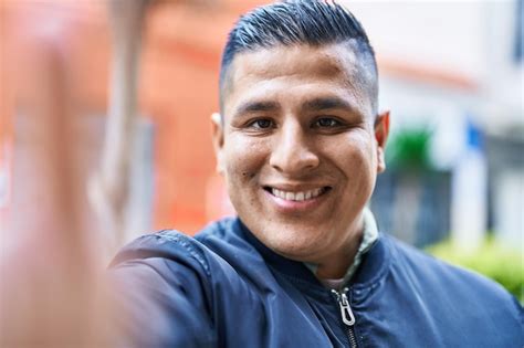 Joven latino sonriendo confiado haciendo selfie por cámara en la calle