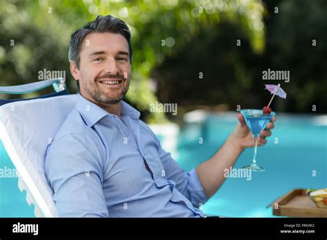 Smart Man Holding Martini Glass While Relaxing In Sun Lounger Stock