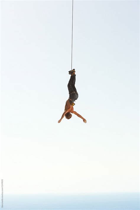 Man Hanging Upside Down With Arms Spread Out From A Rope By Stocksy