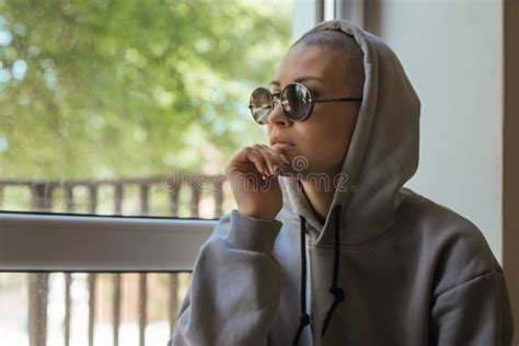 Portrait Of A Young Girl With A Shaved Head In Glasses And A Hood Stock