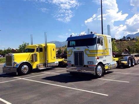 Two Yellow Semi Trucks Parked In A Parking Lot Next To Each Other On A