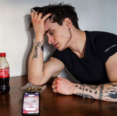 A Man Sitting At A Table With His Hand On His Head And Cell Phone In