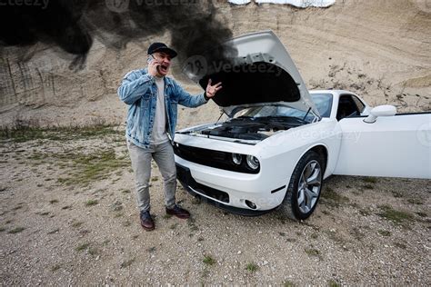 Shocked man calling on phoen to emergency near his broken muscle car