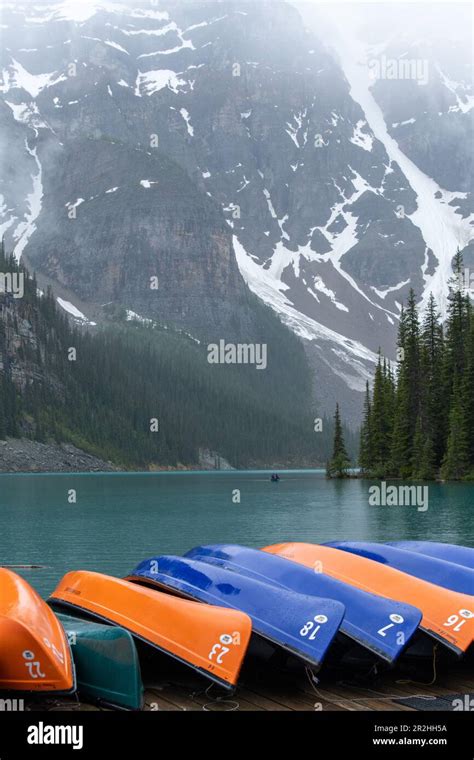 Canoes In Turquoise Lake Louise With Misty Mountains In The Background