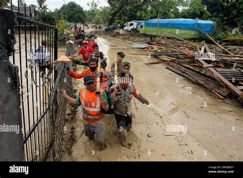 Rescuers Wade Through Mud As They Carry The Body Of A Victim At An Area