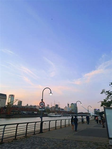 People Are Walking On The Sidewalk Next To The Water At Sunset Or