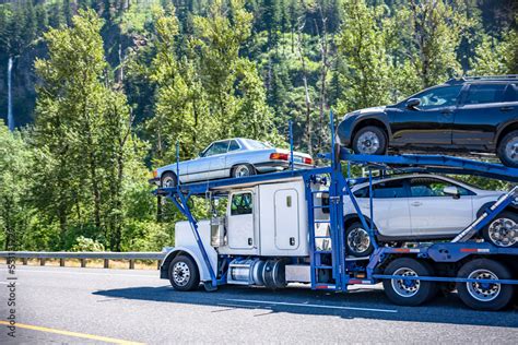 White classic car hauler big rig semi truck with blue modular semi trailer transporting cars ...