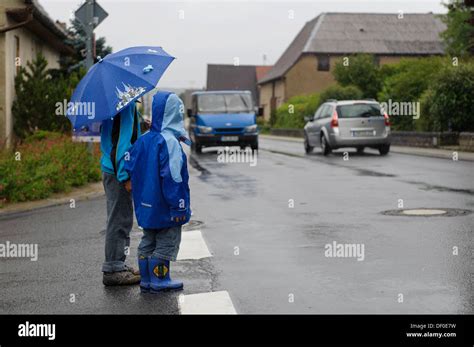 Two children, 4 and 8 years, waiting to cross the street in the rain ...