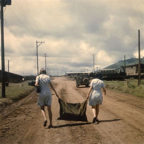 Two People Walking Down A Dirt Road Carrying An Object In The Middle Of