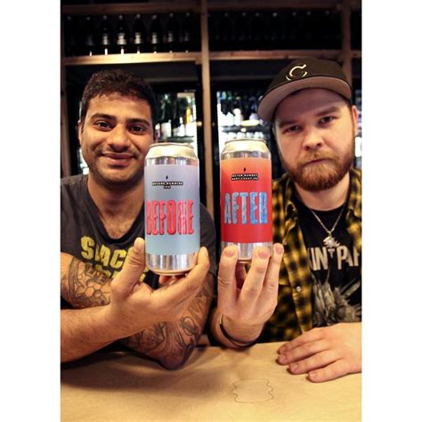 Two Men Sitting At A Table Holding Up Cans Of Beer In Front Of The Camera