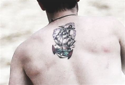 A Man With A Tattoo On His Back Is Standing In The Sand And Looking At
