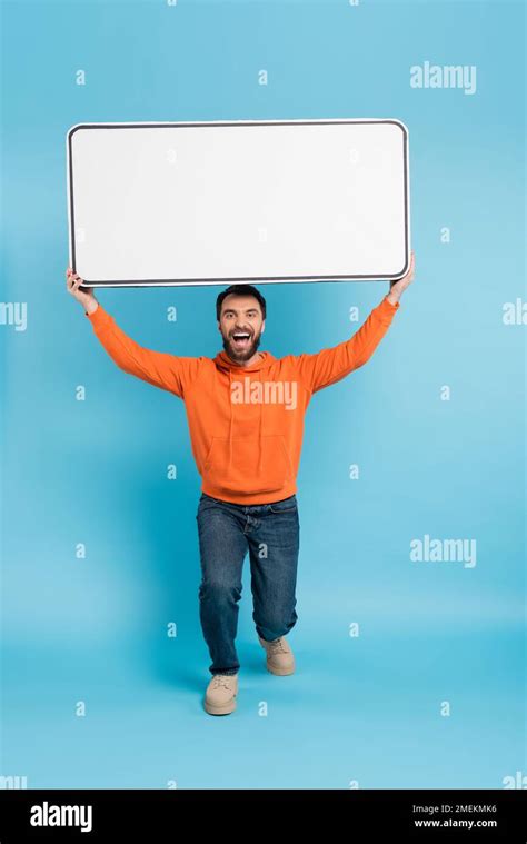 Full Length Of Excited Man In Orange Hoodie And Jeans Holding Big Phone