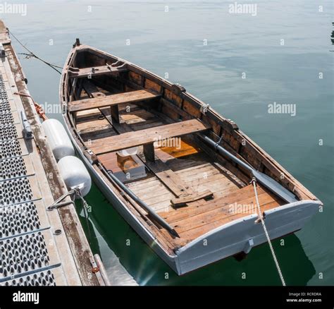 A Wood Row Boat With Some Water In It Is Tied To A Dock On A Clam