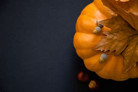 Premium Photo An Orange Pumpkin With Leaves And Acorns On A Black