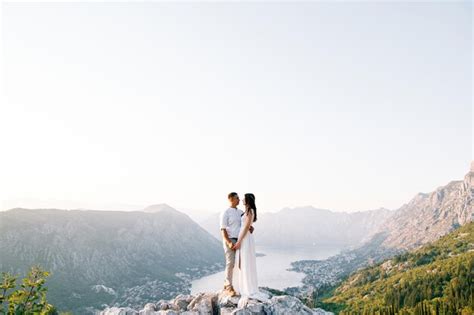 Premium Photo Bride And Groom Stand Hugging On A Rock Above The Bay