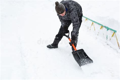 A Man Cleans Snow With A Shovel In Winter In A Swept Yard After A