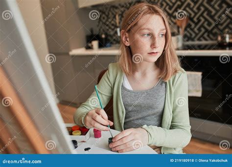 Freckled Girl Looking Away While Painting In Her Home Stock Photo