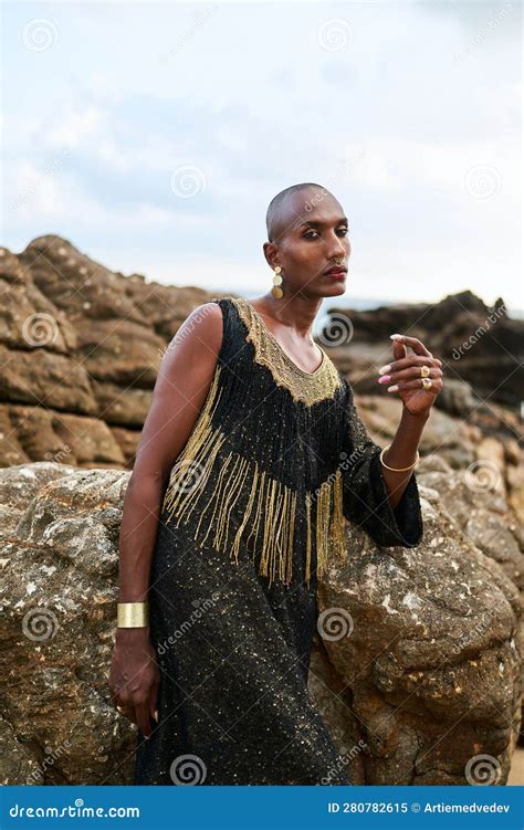 Androgynous Ethnic Fashion Model In Luxury Dress Sits On Rocks By Ocean