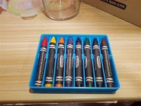 six crayons sitting in a blue container on a table next to a box of other crayons