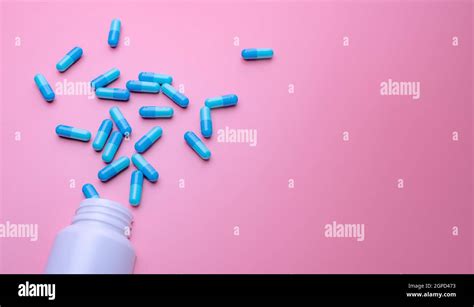 Blue capsule pills spread out of white plastic drug bottle on pink background. Pharmacy banner ...