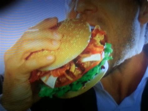 A Man Eating A Giant Hamburger With Bacon And Lettuce