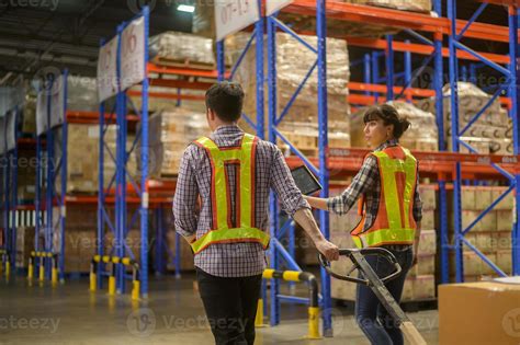 Young factory workers pulling a pallet truck between shelves full of