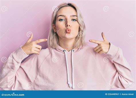 Young Blonde Girl Pointing Mouth With Fingers Looking At The Camera Blowing A Kiss Being Lovely