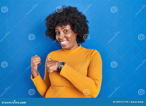 Black Woman With Curly Hair Standing Over Blue Background Pointing To The Back Behind With Hand