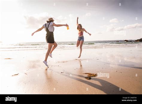 Two Girlfriends Having Fun Running And Jumping On The Beach Stock